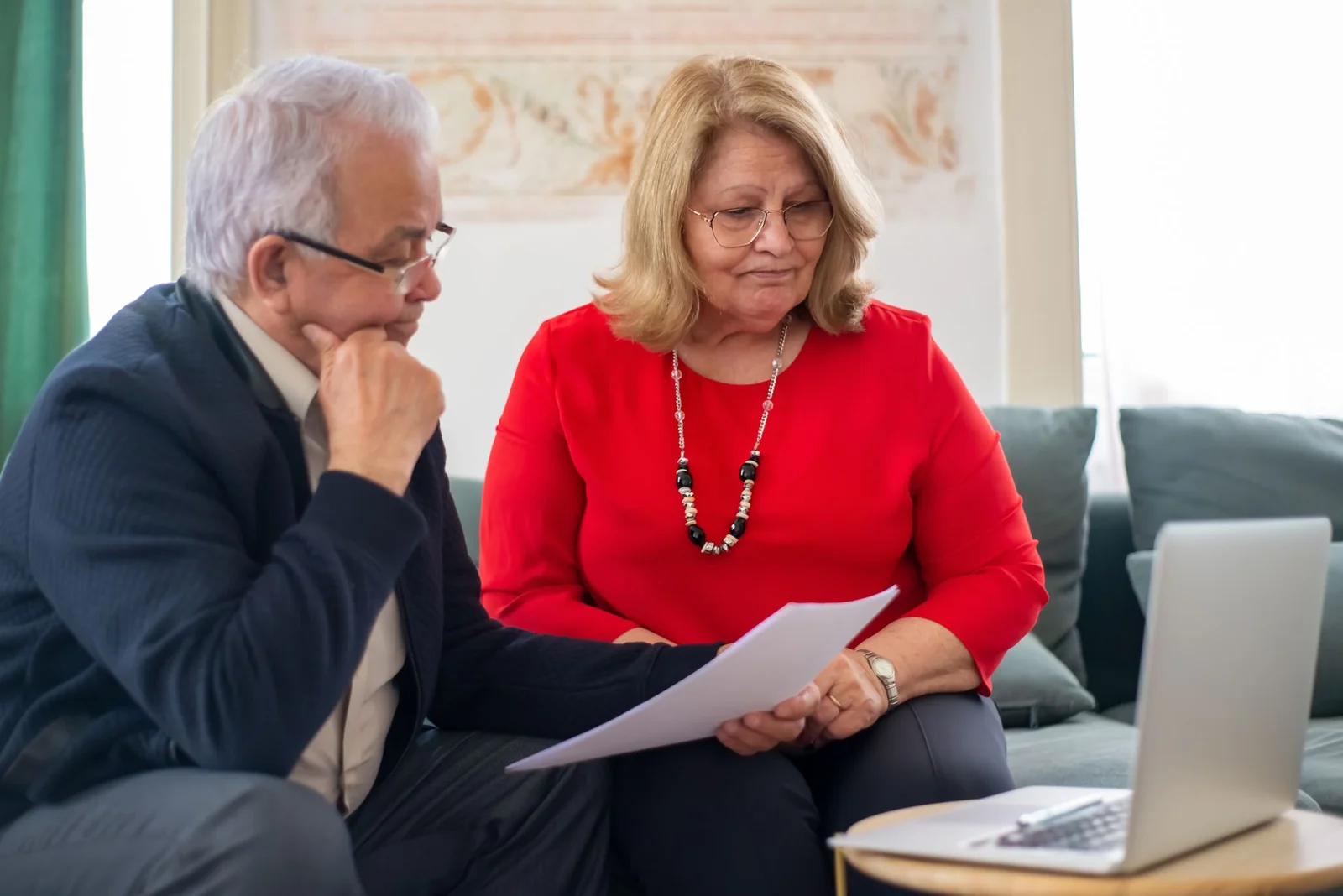 Couple examinant des documents d'investissement sur une table de salon avec un ordinateur portable